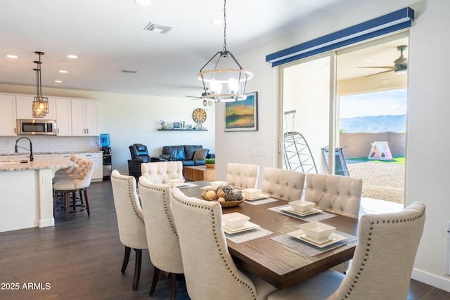 dining space featuring ceiling fan with notable chandelier, dark hardwood / wood-style flooring, a mountain view, and sink