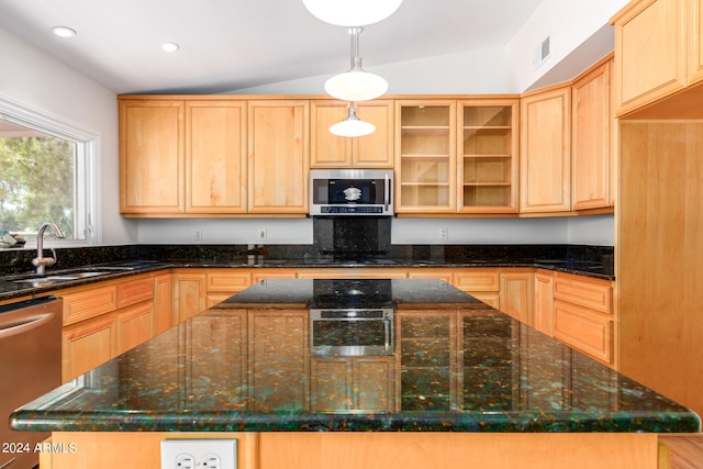 kitchen with appliances with stainless steel finishes, a center island, dark stone counters, and vaulted ceiling