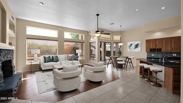 living room with light tile patterned flooring, sink, a towering ceiling, ceiling fan, and a fireplace