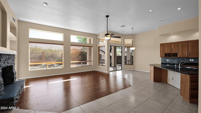 kitchen with tasteful backsplash, hanging light fixtures, light tile patterned floors, ceiling fan, and a fireplace