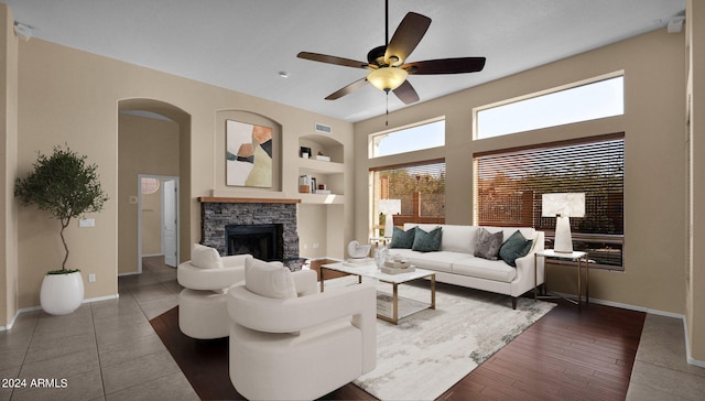 living room featuring a stone fireplace, ceiling fan, and built in shelves