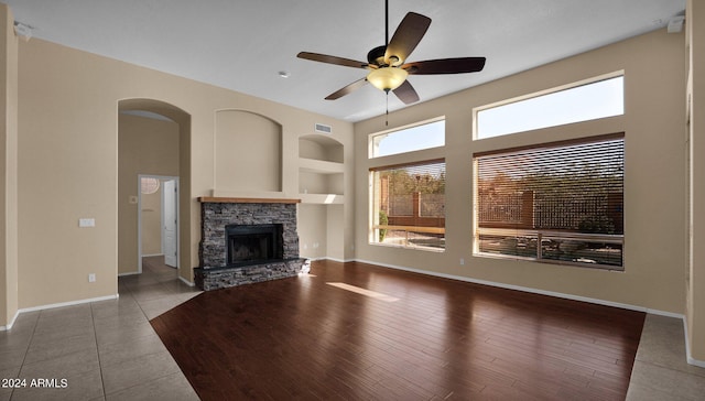 unfurnished living room with a stone fireplace, built in features, ceiling fan, and tile patterned floors