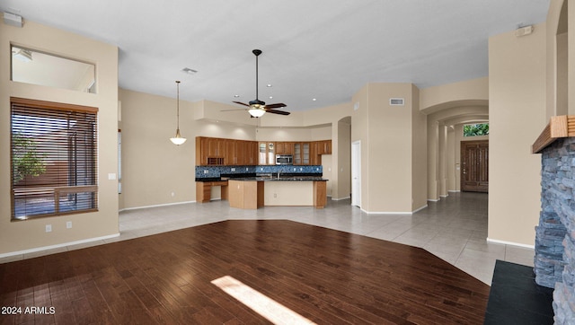 unfurnished living room with a high ceiling, sink, ceiling fan, and light hardwood / wood-style floors