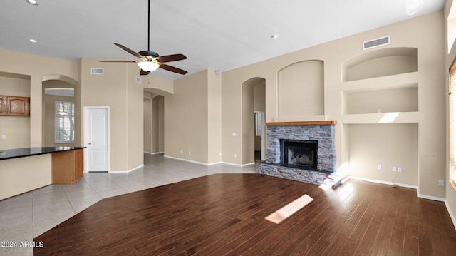 unfurnished living room featuring ceiling fan, built in shelves, a fireplace, and light hardwood / wood-style floors