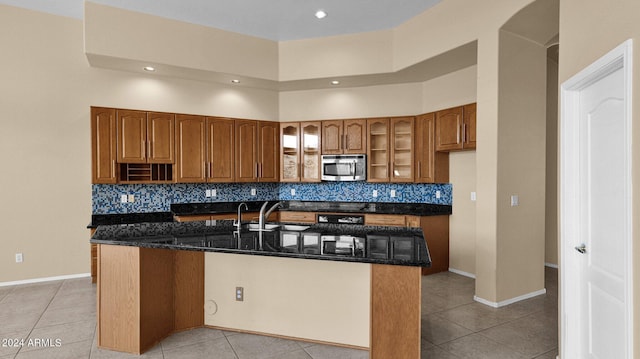 kitchen featuring dark stone countertops, a towering ceiling, light tile patterned floors, and a kitchen island with sink