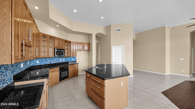 kitchen with sink, a center island with sink, oven, and light tile patterned floors