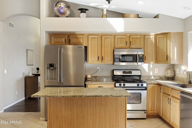 kitchen with sink, a kitchen island, light tile patterned floors, and appliances with stainless steel finishes