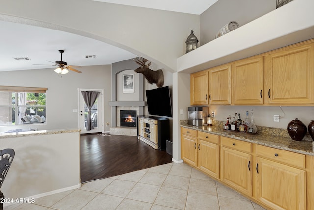 kitchen with light brown cabinetry, ceiling fan, light hardwood / wood-style flooring, lofted ceiling, and a tiled fireplace