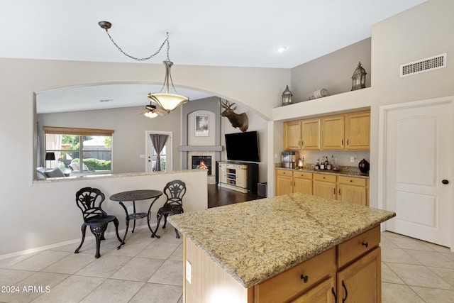 kitchen featuring vaulted ceiling, pendant lighting, a fireplace, a center island, and light tile patterned flooring