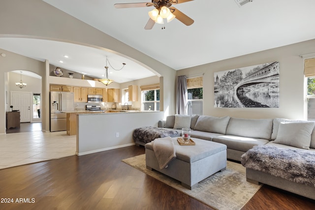 living room with ceiling fan with notable chandelier, light hardwood / wood-style flooring, vaulted ceiling, and sink