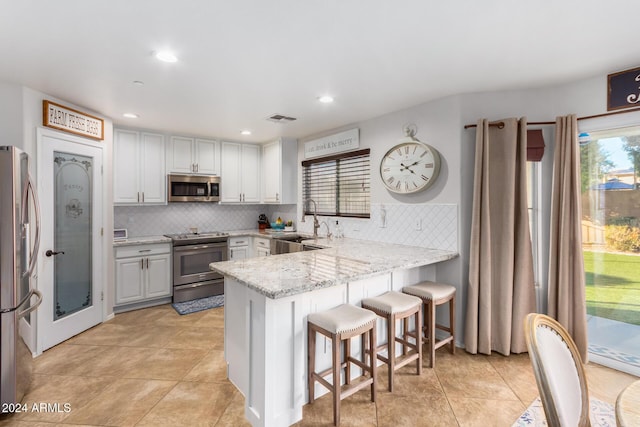 kitchen with kitchen peninsula, appliances with stainless steel finishes, decorative backsplash, a kitchen breakfast bar, and white cabinetry