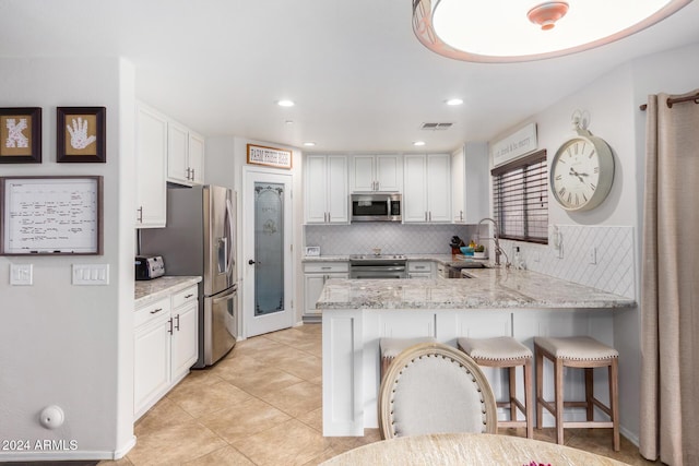 kitchen with a kitchen bar, appliances with stainless steel finishes, kitchen peninsula, light stone countertops, and white cabinets