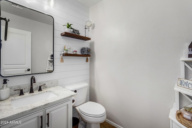 bathroom featuring vanity, wood walls, and toilet