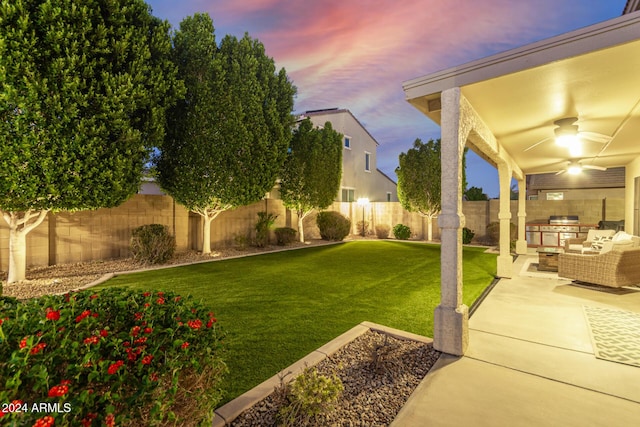 yard at dusk featuring a patio area, ceiling fan, and exterior kitchen