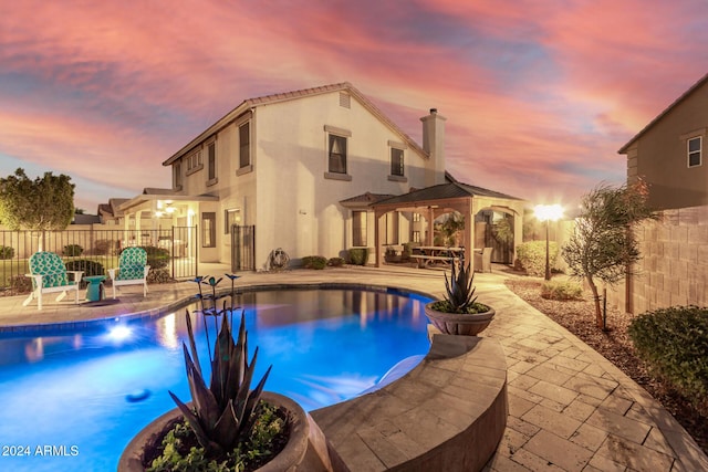 pool at dusk with a gazebo and a patio area