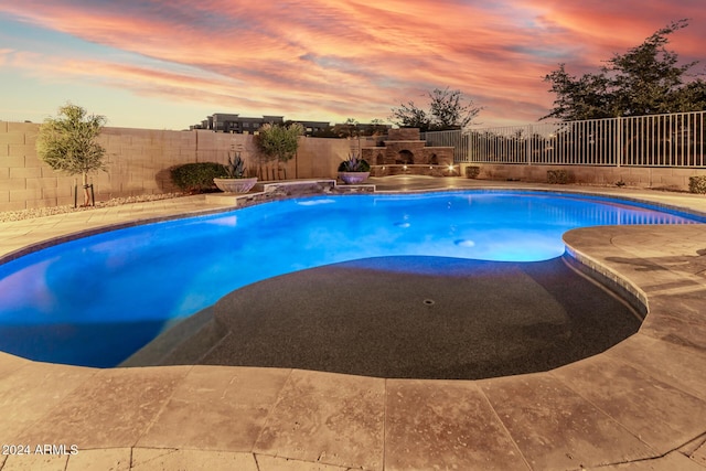 pool at dusk with a patio area and exterior fireplace