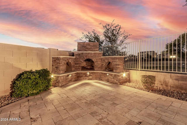 patio terrace at dusk featuring an outdoor stone fireplace