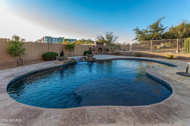 view of pool featuring pool water feature, an outdoor stone fireplace, and a patio area