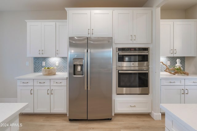 kitchen with white cabinetry, stainless steel appliances, light hardwood / wood-style floors, and backsplash