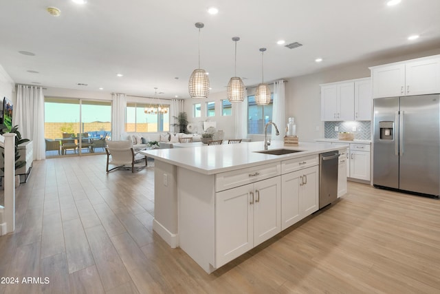 kitchen featuring decorative light fixtures, white cabinetry, an island with sink, sink, and stainless steel appliances