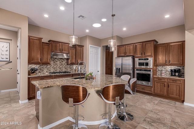 kitchen with light stone countertops, sink, pendant lighting, a center island with sink, and appliances with stainless steel finishes