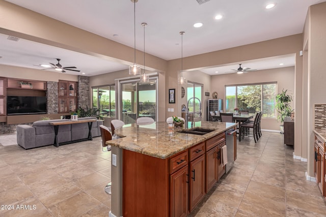 kitchen featuring light stone counters, ceiling fan, sink, pendant lighting, and an island with sink