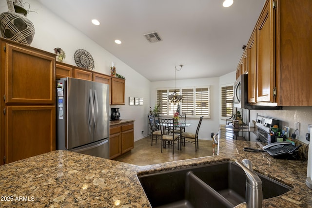 kitchen with appliances with stainless steel finishes, dark stone counters, pendant lighting, an inviting chandelier, and lofted ceiling