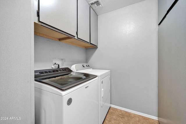 laundry room featuring washing machine and clothes dryer, light tile patterned floors, and cabinets