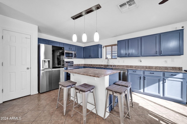 kitchen with a breakfast bar, blue cabinets, light tile patterned floors, appliances with stainless steel finishes, and decorative light fixtures