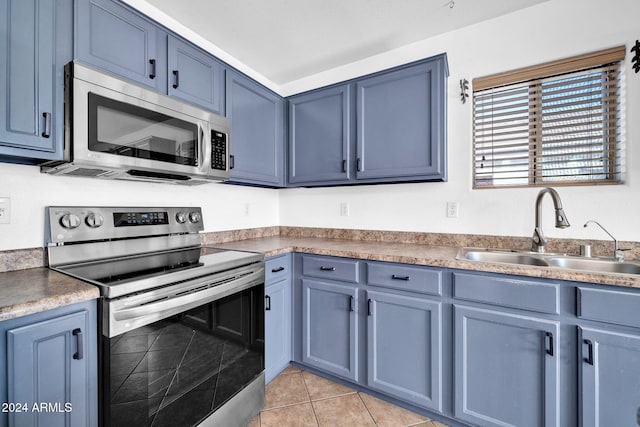 kitchen with light tile patterned floors, stainless steel appliances, blue cabinets, and sink