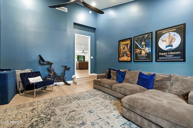 living area featuring wood finished floors, visible vents, a towering ceiling, a ceiling fan, and baseboards