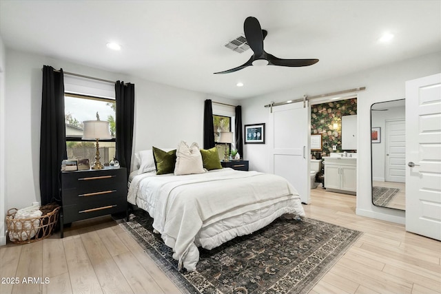 bedroom with light wood-type flooring, a barn door, visible vents, and recessed lighting