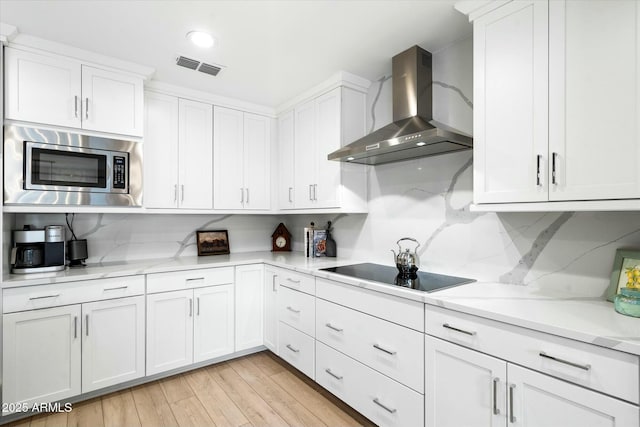 kitchen featuring light wood finished floors, stainless steel microwave, visible vents, wall chimney exhaust hood, and black electric cooktop