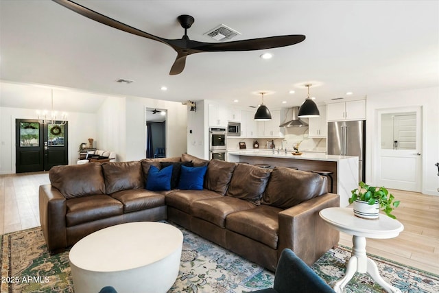 living area featuring light wood-style floors, ceiling fan with notable chandelier, visible vents, and recessed lighting