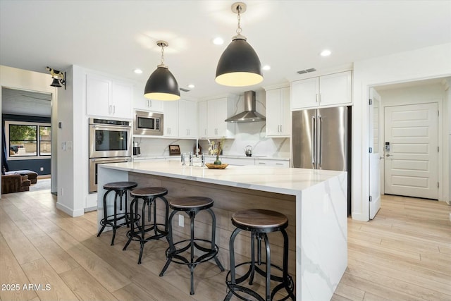 kitchen with white cabinetry, light wood-style floors, wall chimney exhaust hood, and appliances with stainless steel finishes