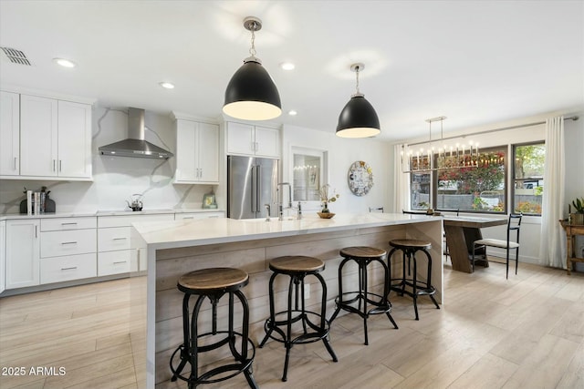 kitchen with high end refrigerator, visible vents, light wood-style floors, light countertops, and wall chimney exhaust hood