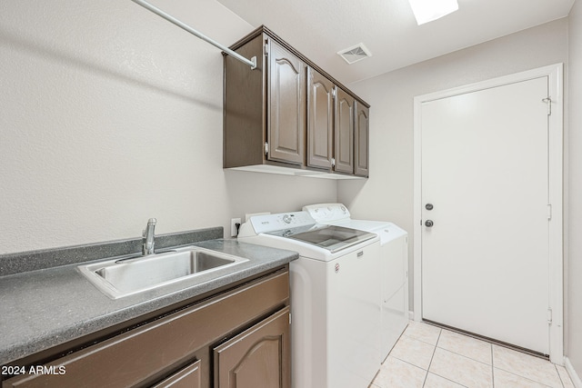 clothes washing area featuring washer and clothes dryer, sink, light tile patterned floors, and cabinets