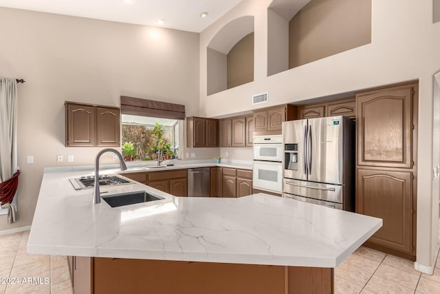 kitchen featuring kitchen peninsula, a high ceiling, stainless steel appliances, and light tile patterned floors