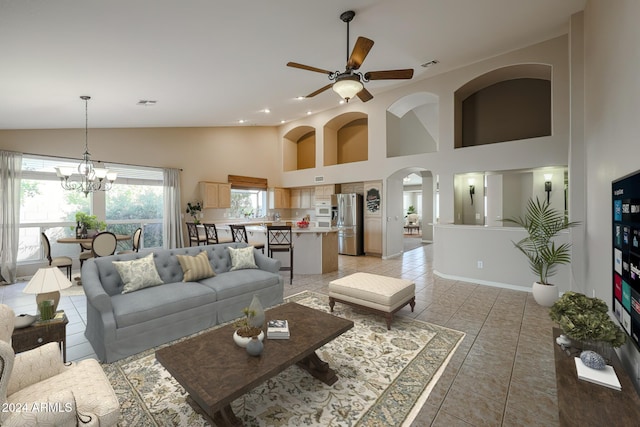 tiled living room featuring high vaulted ceiling and ceiling fan with notable chandelier