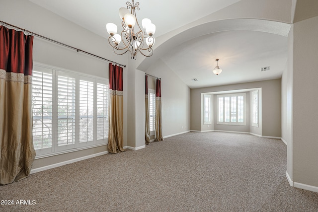 empty room with carpet floors, an inviting chandelier, vaulted ceiling, and a healthy amount of sunlight