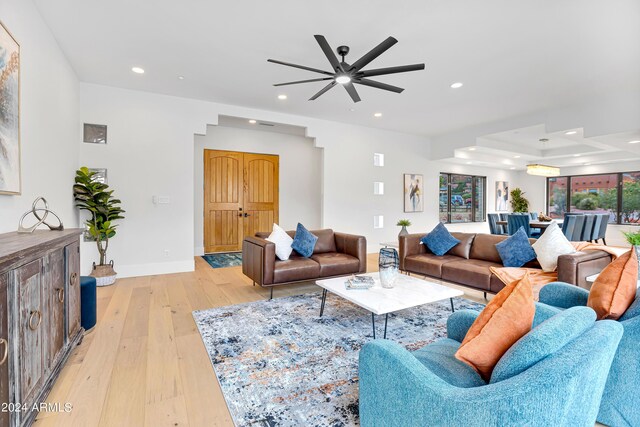 living room with a tray ceiling, light wood-style flooring, recessed lighting, and baseboards