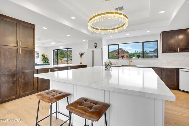 kitchen with light wood-type flooring, a raised ceiling, white appliances, and a center island