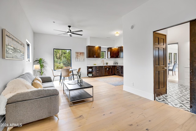 living area featuring light wood finished floors, baseboards, and ceiling fan