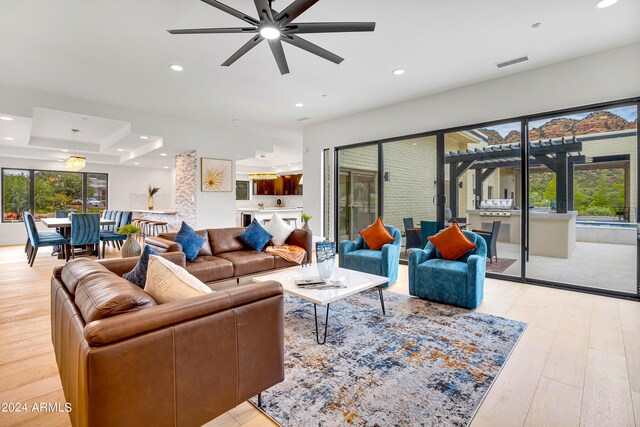 living room featuring visible vents, a tray ceiling, recessed lighting, light wood-style flooring, and a ceiling fan