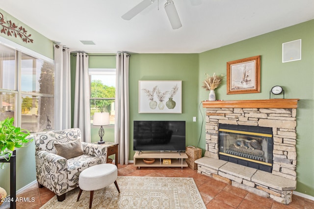 tiled living room featuring ceiling fan and a stone fireplace