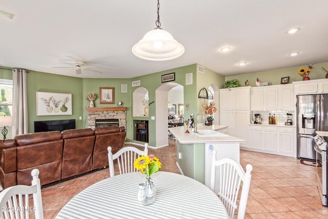 dining area with a stone fireplace, ceiling fan, sink, and light tile patterned floors