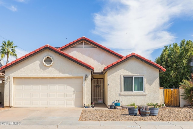 view of front of property with stucco siding, fence, a garage, driveway, and a tiled roof