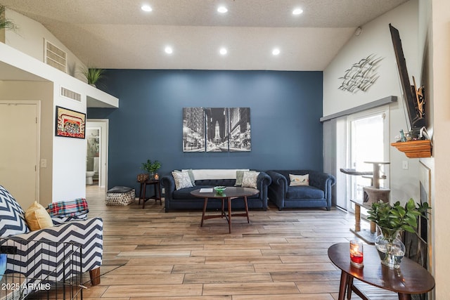 living area with a towering ceiling, wood finished floors, visible vents, and recessed lighting