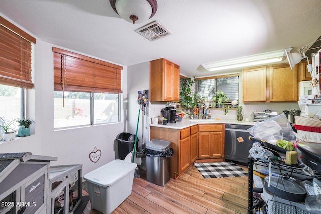 kitchen featuring light countertops, visible vents, light wood-style floors, a sink, and dishwasher