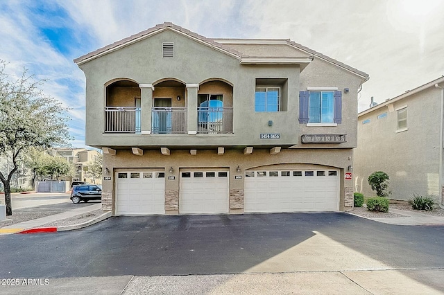 townhome / multi-family property featuring a balcony, a garage, aphalt driveway, and stucco siding